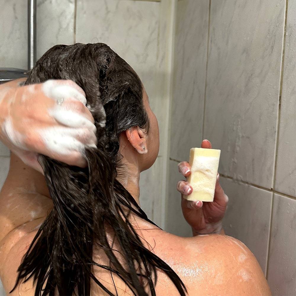 Femme dans la douche qui se lave les cheveux tout en présentant le produit UltraPouss
