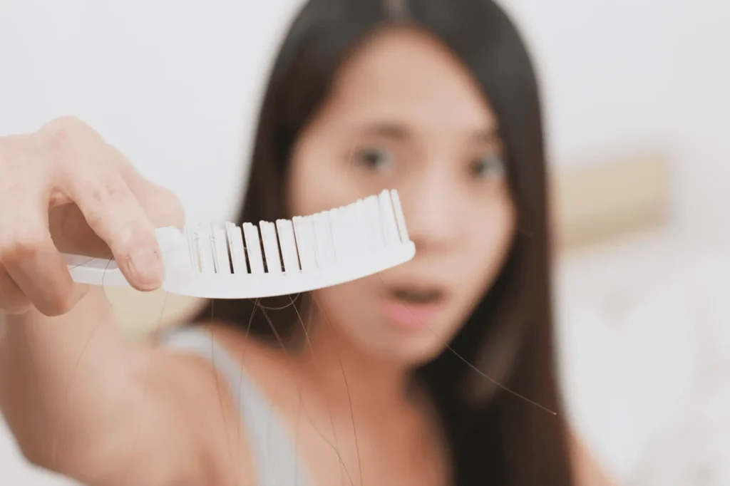 Femme qui montre une brosse où on y voit des cheveux tombés